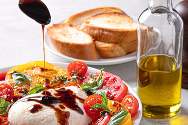 Cheese drizzled with balsamic vinegar next to tomatoes, bread and olive oil
