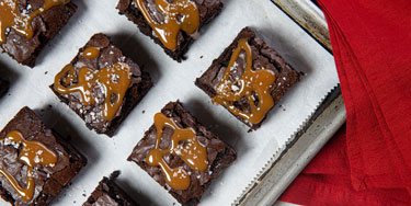 Brownies topped with caramel and flake salt next to red napkins