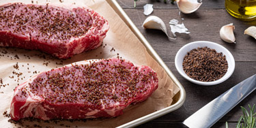 Two steaks with smoked salt dry rub next to ingredients and knife